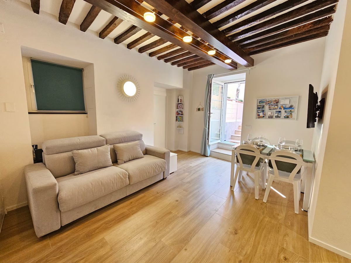 Soggiorno luminoso con divano, travi in legno e zona pranzo