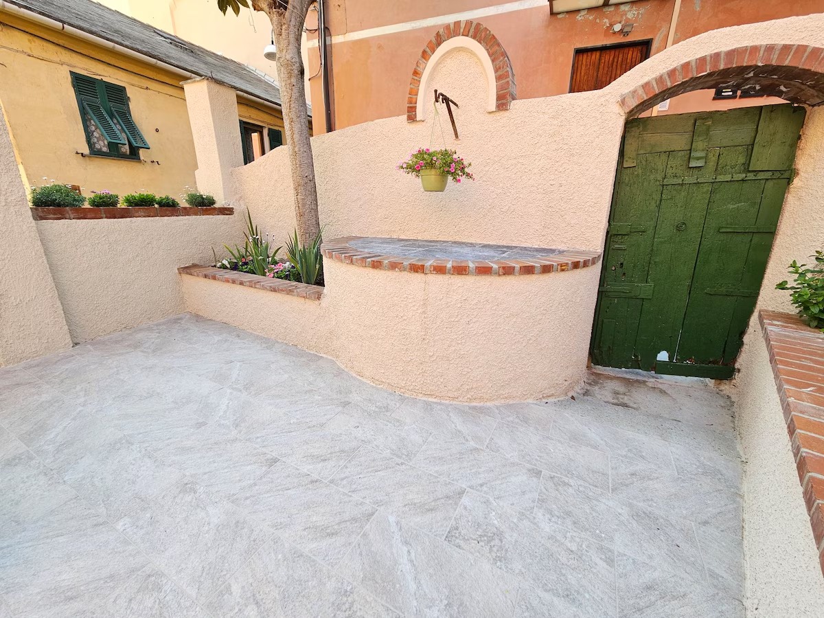 Cortile pavimentato con aiuole fiorite e antico portone verde